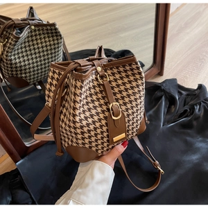 Detail of houndstooth bucket bag featuring brown leather trim and drawstring closure