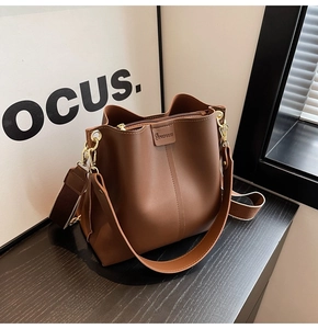 Detail of a brown bucket bag showing fine leather texture and golden metal buckle