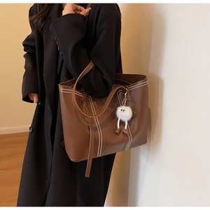 Brown tote bag with white stitching detail and fluffy charm on a model's shoulder