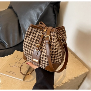 Close-up of brown houndstooth bucket bag with leather trim on a vintage stone base