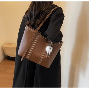 Detail of a brown tote bag with white contrast stitching and a white plush charm