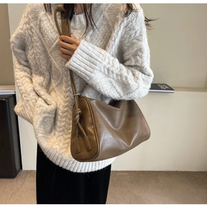 Detail of tan leather crossbody bag featuring unique knot decor on shoulder strap