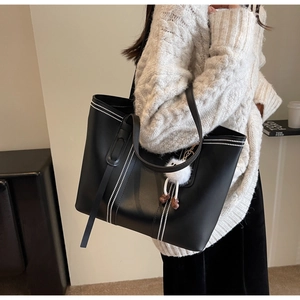 Close-up of black tote bag featuring white vertical stitching and a plush ball charm