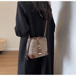 Detail of houndstooth bucket bag featuring brown leather trim and gold metal buckle