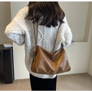 Detail view of large brown leather tote with a stylish knot handle worn on a white sweater