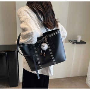 Detail view of a black leather tote bag with silver beaded decor and a white plush charm