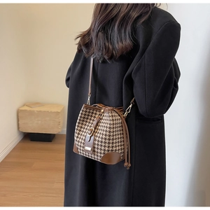 Detail of houndstooth bucket bag with brown leather trim worn by model in black coat