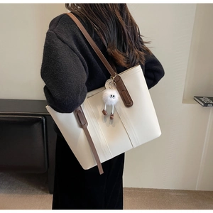 Detail of off-white tote bag featuring contrast straps and a plush monster charm
