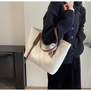 Detail of the large white tote bag with brown straps and a decorative plush pom-pom charm