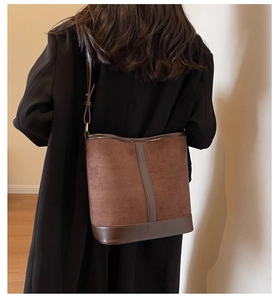 Detail view of large brown suede bucket bag with leather trim on model in black coat