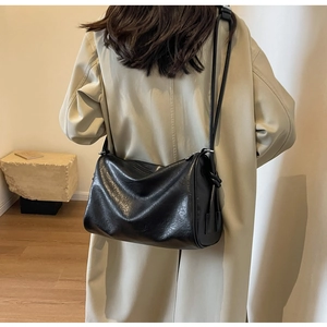 Detail of black glossy cylindrical shoulder bag worn with a chic beige trench coat
