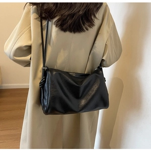 Detail shot of a black minimalist Boston bag with knotted straps worn with a beige coat