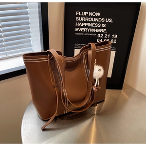 Brown leather tote bag featuring white dotted stitching and a plush smiley face charm