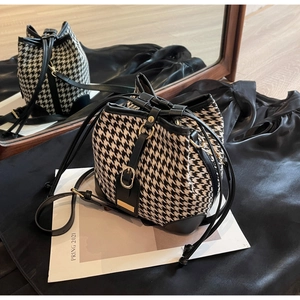 Detail of houndstooth bucket bag with black leather trim, drawstring, and gold hardware
