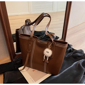 Detailed view of brown leather tote bag with white stitching and plush monster charm