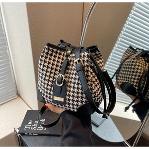 Detail of houndstooth bucket bag with black leather trim and golden metal tag decoration