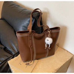 Detail of coffee brown leather tote with white stitching and plush monster charm