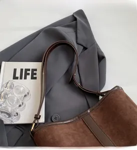 Detail of brown suede tote bag with leather trim and adjustable strap on grey blazer