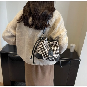 Detail of houndstooth bucket bag with leather trim and drawstring on a beige sweater
