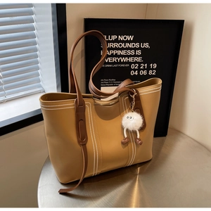 Detail view of large light brown tote bag with white contrast stitching and plush charm