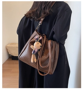 Detail of brown woven tote bag featuring a plush rabbit charm and detachable shoulder strap