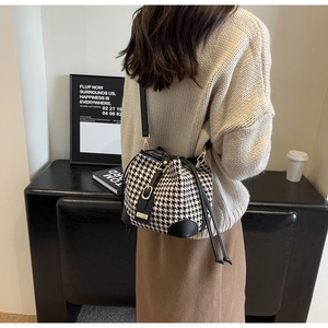 Detail of houndstooth bucket bag with black leather trim and drawstring on a model