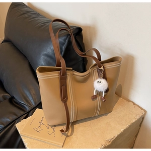 Detail of khaki leather tote with brown handles and a cute fuzzy white monster charm