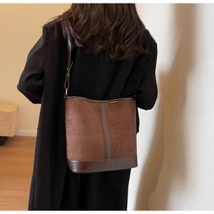 Detail of a large brown bucket bag in matte finish with smooth leather trim on a model