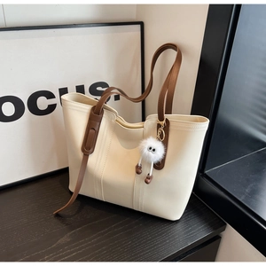 Large cream tote bag with brown straps and plush ball charm on a sleek dark surface