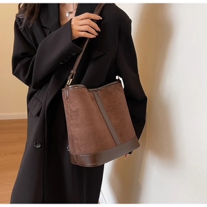 Detail showing the brown suede texture and smooth leather trim of the bucket bag