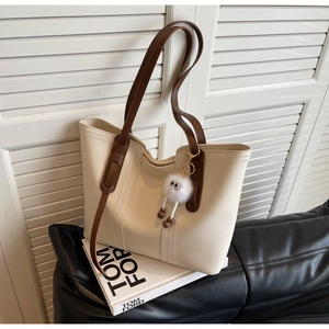 Detail of a large cream tote bag with dark brown straps and a plush doll pendant accessory