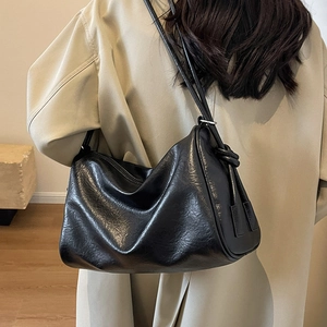 Chic black leather tote bag with knotted side details on beige trench coat model