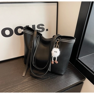 Detail of black matte PU leather tote bag with white contrast stitching and plush charm