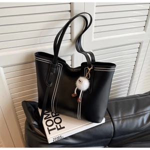 Close-up of black leather tote bag featuring white dot stitching and furry ball charm