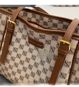 Close-up of beige jacquard tote bag featuring leather handles and golden metal buckles