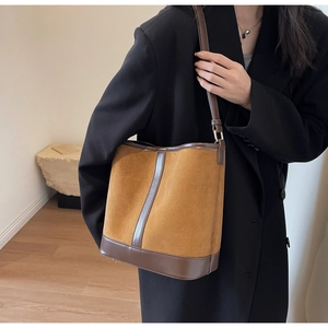 Brown suede bucket bag shown on shoulder, matching a black blazer for a retro style