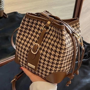 Chic houndstooth bucket bag with brown leather trim and adjustable strap held by hand