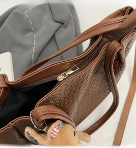 Detail of a brown woven tote bag featuring a smooth gold zipper and a cute plush charm