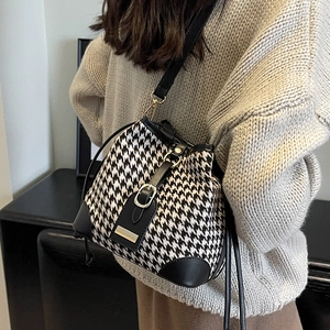 Chic houndstooth bucket bag with leather trim and gold buckle shown on model