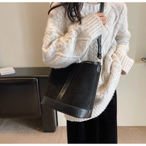 Detail of black suede and leather bucket bag with adjustable strap worn by a model