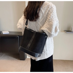 Detail of black suede and leather bucket bag worn with a white knitted sweater