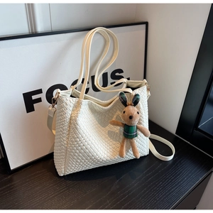 Macro shot of white woven texture tote bag featuring a cute bunny plush charm on the side