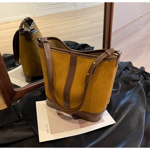 Detail of vintage yellow suede bucket bag with contrast brown leather trim and metal rivets