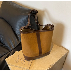 Detail view of caramel suede and brown leather bucket bag on a minimalist stone display
