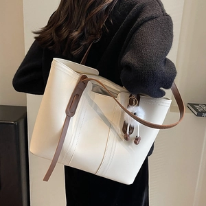 Minimalist beige tote bag with brown straps and plush charm shown on female shoulder