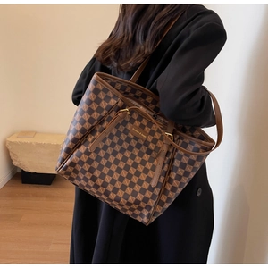 Detail of checkered tote bag with brown pattern and leather label on shoulder
