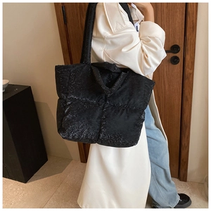 Dettaglio borsa tote nera trapuntata con finitura glitter indossata con trench coat