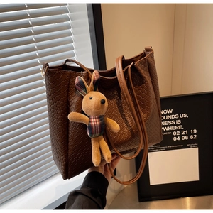 Detail of woven brown leather tote bag featuring a cute rabbit charm and dual shoulder straps