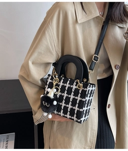 Dettaglio della borsa in tweed a scacchi con dettagli dorati e ciondolo su un trench coat