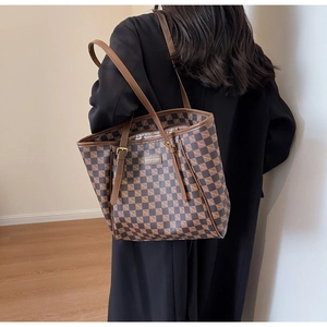 Detailed view of brown checkered tote bag with leather handles shown on shoulder